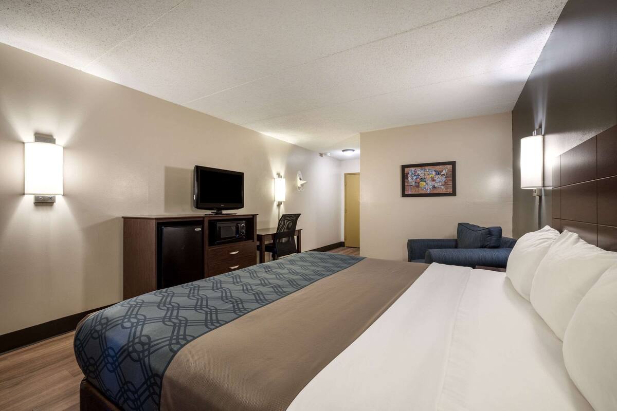 A hotel room with a bed, a desk with a television, a chair, and a couch.
