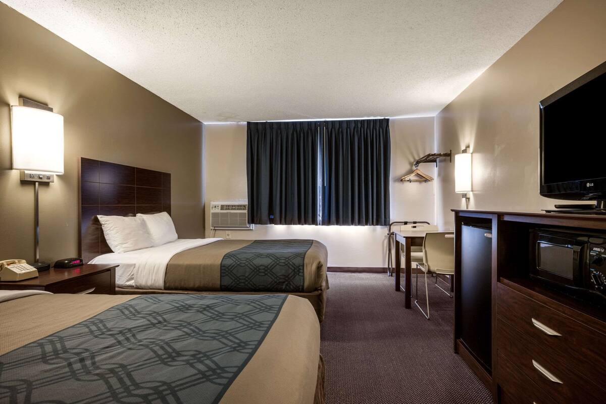 A hotel room with two beds, a desk, a TV, and a minibar.