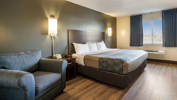 A hotel room with a bed, a sofa, a nightstand with a phone, two wall-mounted lamps, and a window with curtains. - Econo Lodge Darien Lakes (Corfu)