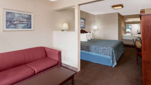 A hotel room with a red sofa, a bed with patterned bedding, a desk, and a painting on the wall. - Days Inn by Wyndham Morristown (Morristown)