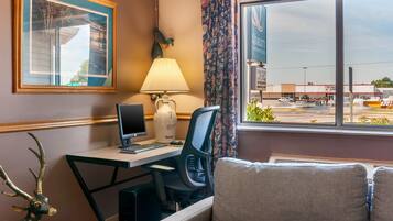 Habitación de hotel con escritorio, computadora, lámpara y vista a un estacionamiento.