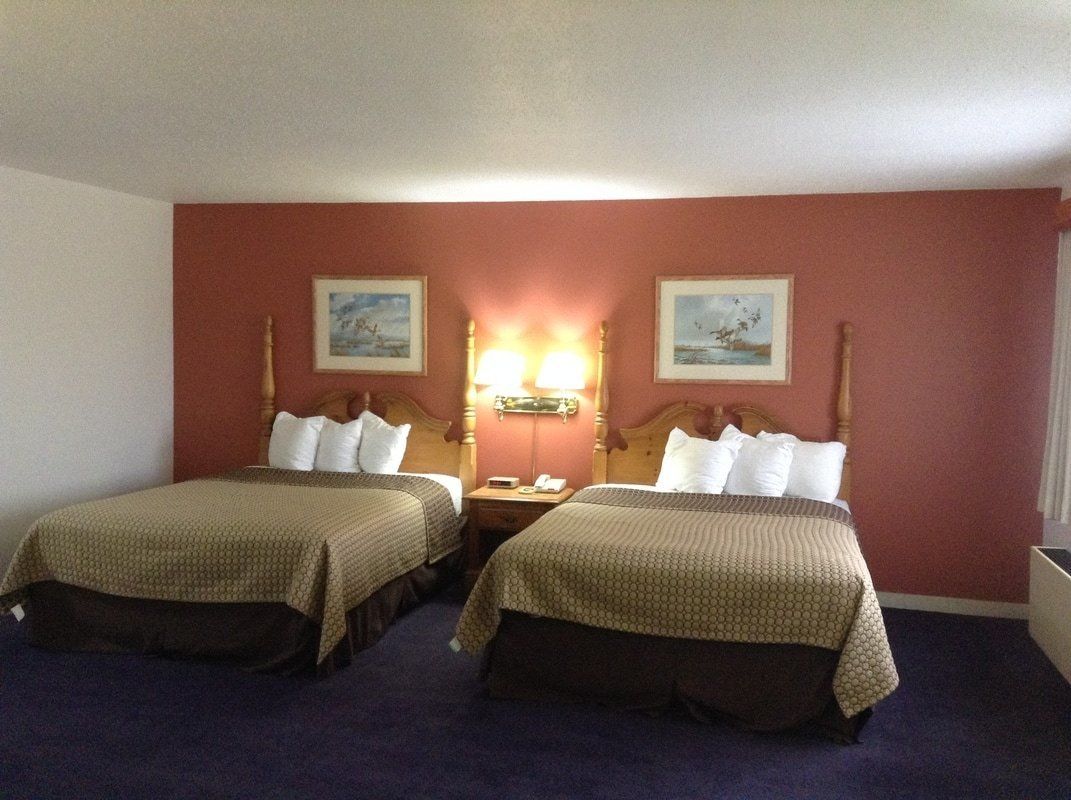 A hotel room with two beds, a nightstand, a lamp, and two framed pictures on the wall.