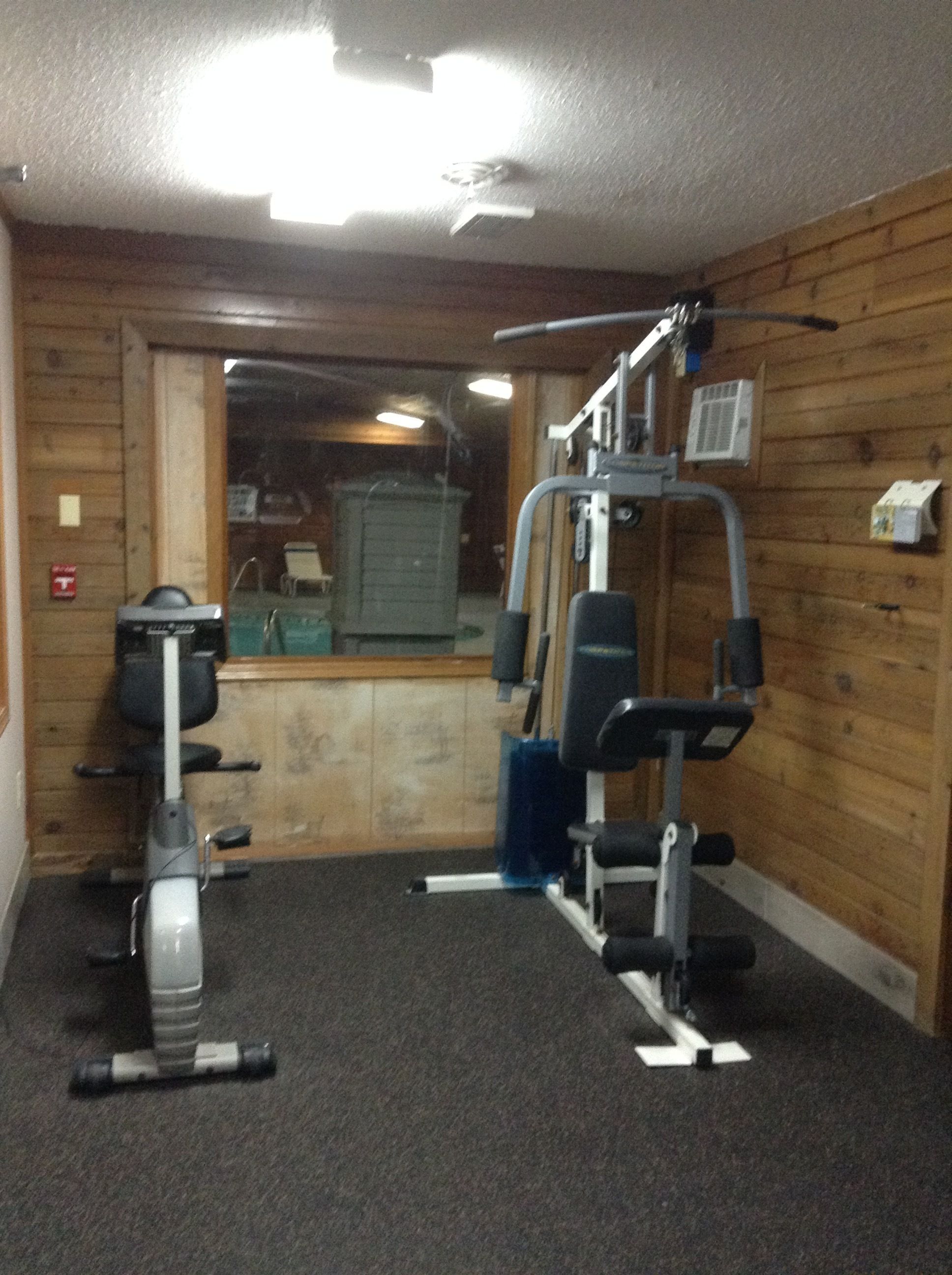 Academia com equipamentos de ginástica, paredes de madeira e uma janela.