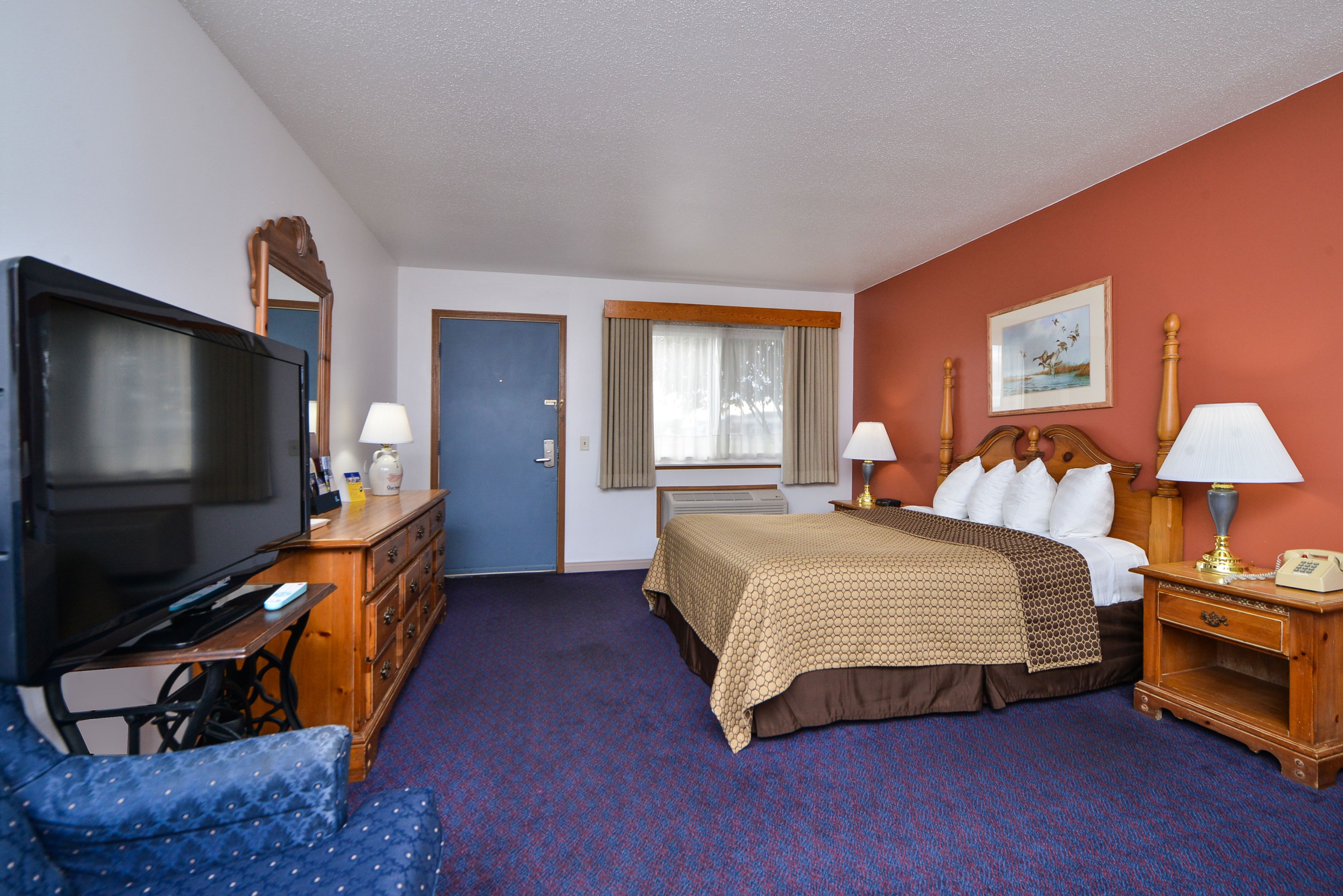 A hotel room with a bed, a television, a desk with a lamp, and a chair.