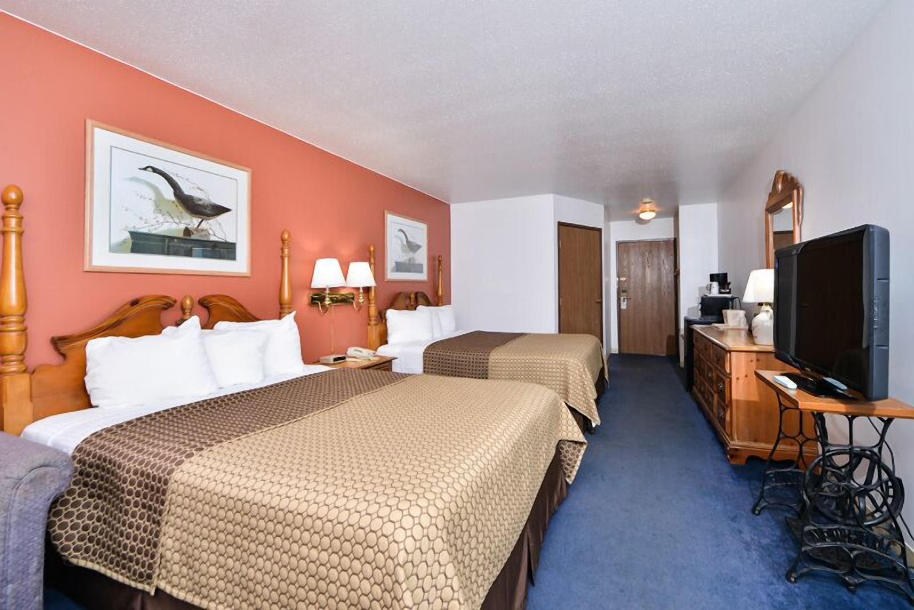 A hotel room with two beds, a television, a dresser, and artwork on the walls.