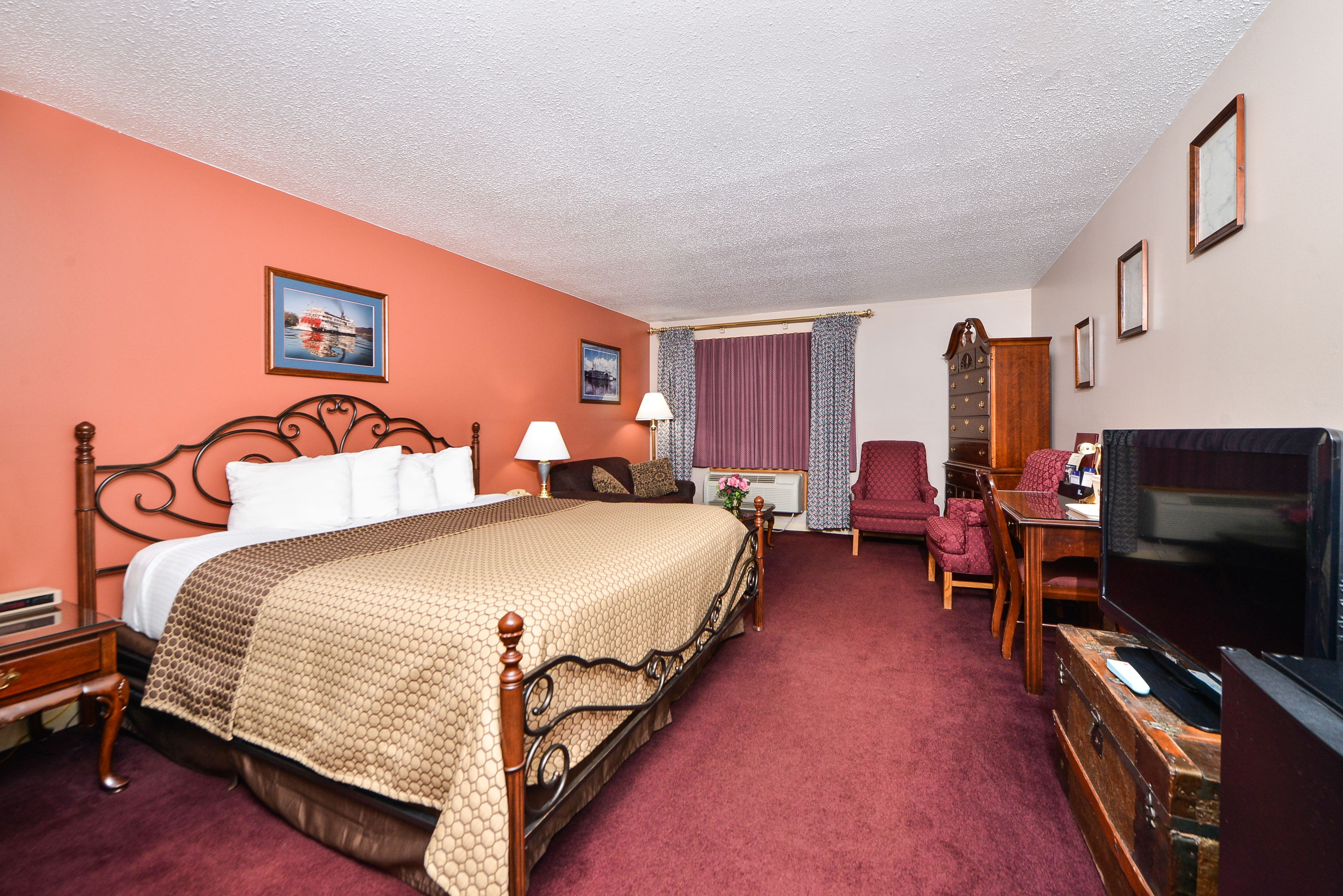 A hotel room with a large bed, a television, a desk with a chair, and a wardrobe.