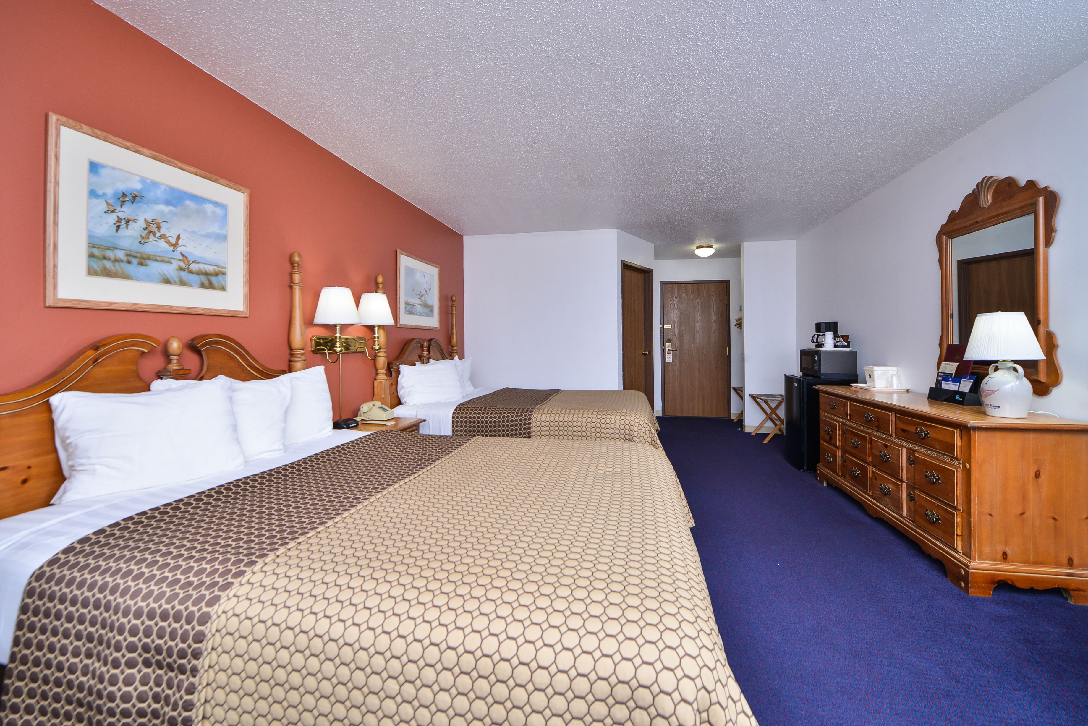 A hotel room with two beds, a wooden dresser, a desk, and a mirror.