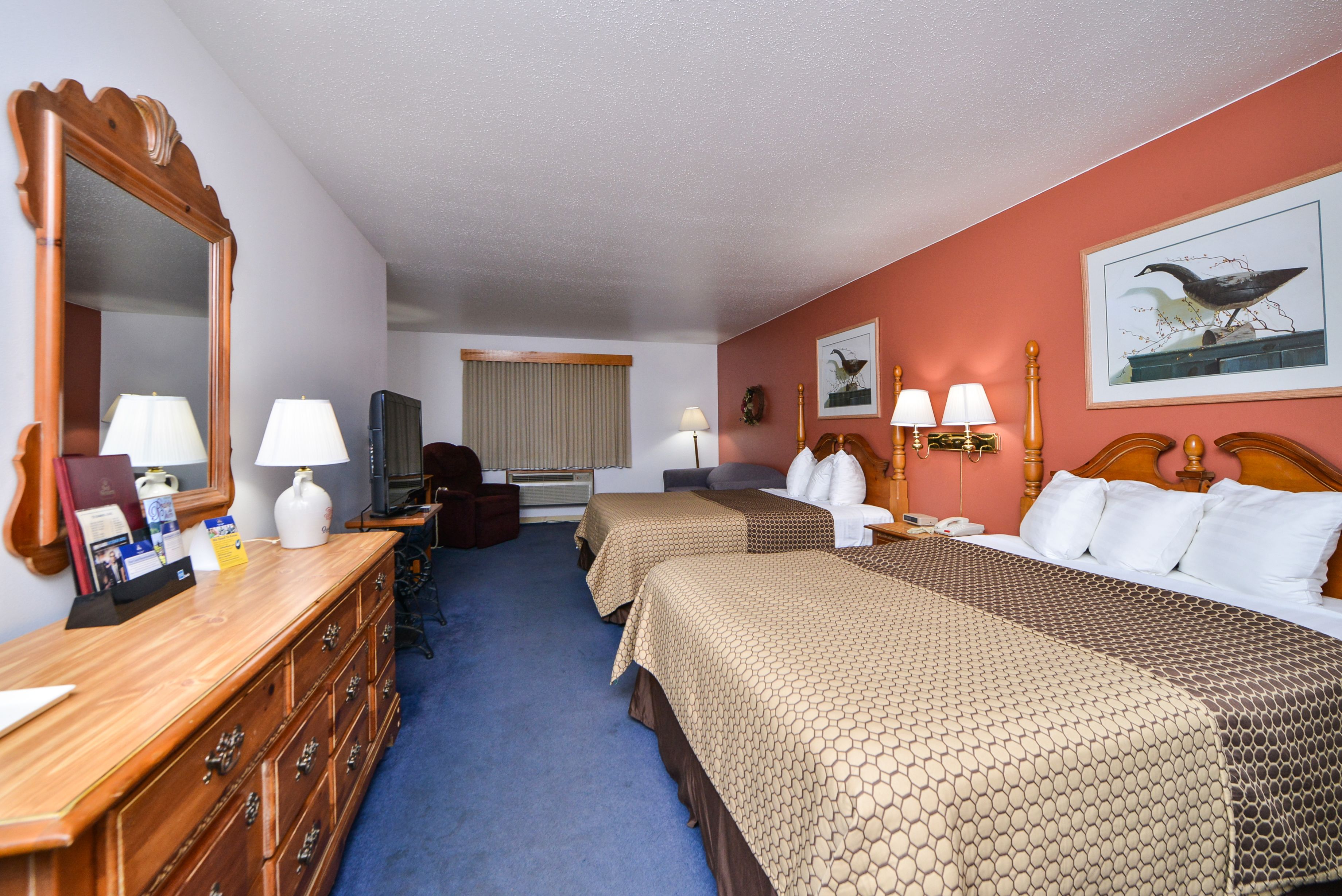 A hotel room with two beds, a dresser, a mirror, a television, and a window with curtains.