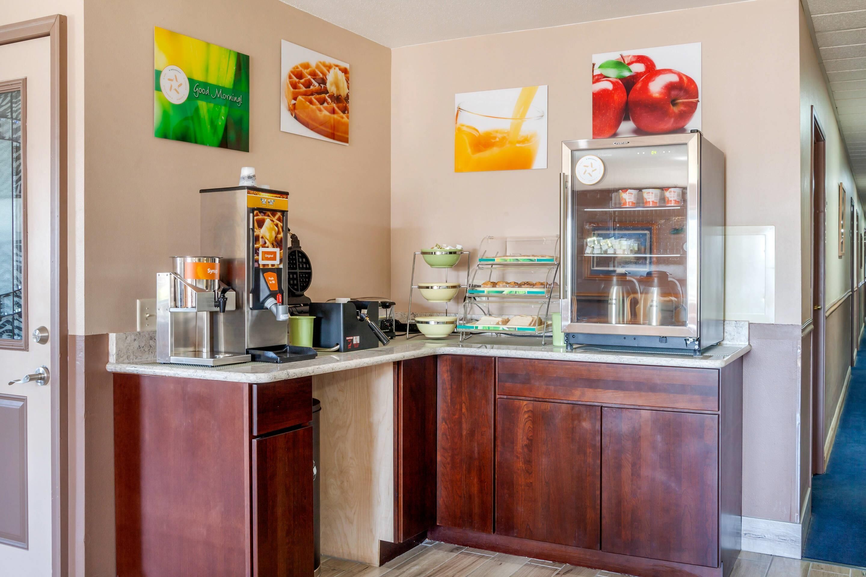 Une cuisine d’hôtel équipée d’une machine à café, d’un appareil à gaufres et d’un réfrigérateur rempli de boissons.