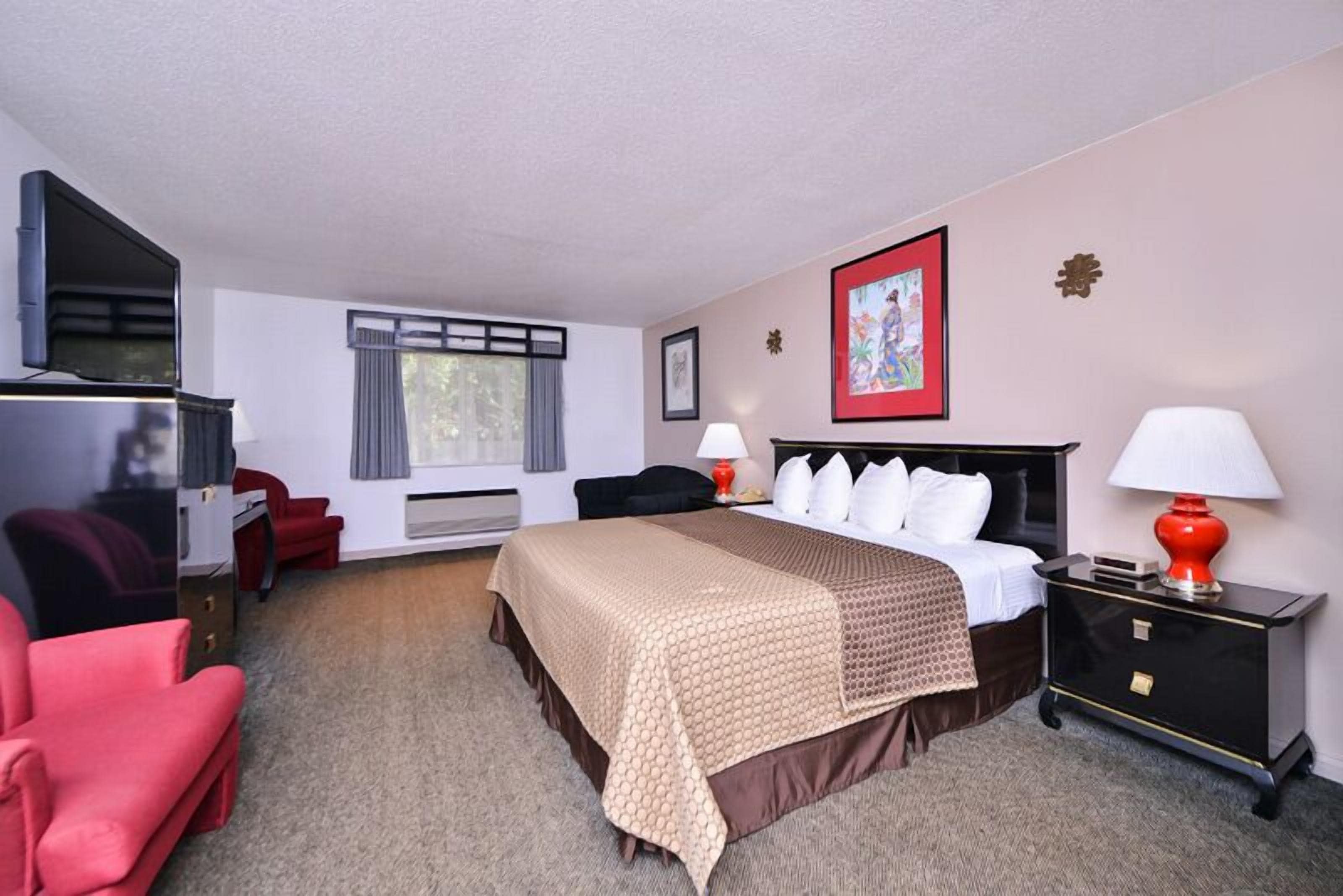 Habitación de hotel con cama, escritorio, silla, televisión y ventana con cortinas.