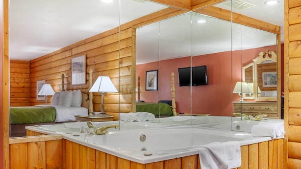 A wooden cabin-style room with a large mirror, a bed, a vanity with a mirror, and a bathtub. - Quality Inn & Suites Prairie Du Chien (Prairie Du Chien)