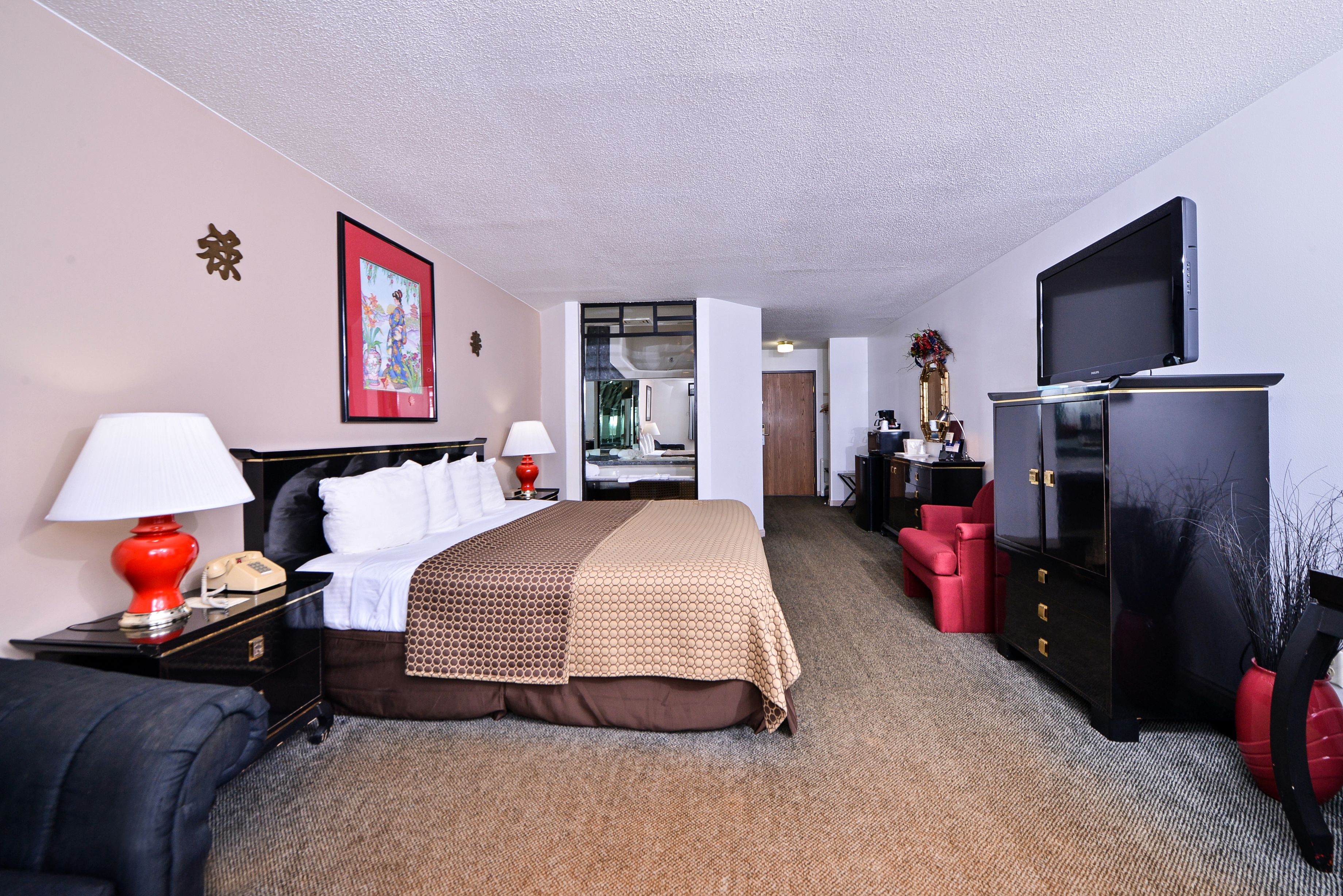 Habitación de hotel con cama, televisor, escritorio, lámpara y una silla roja.