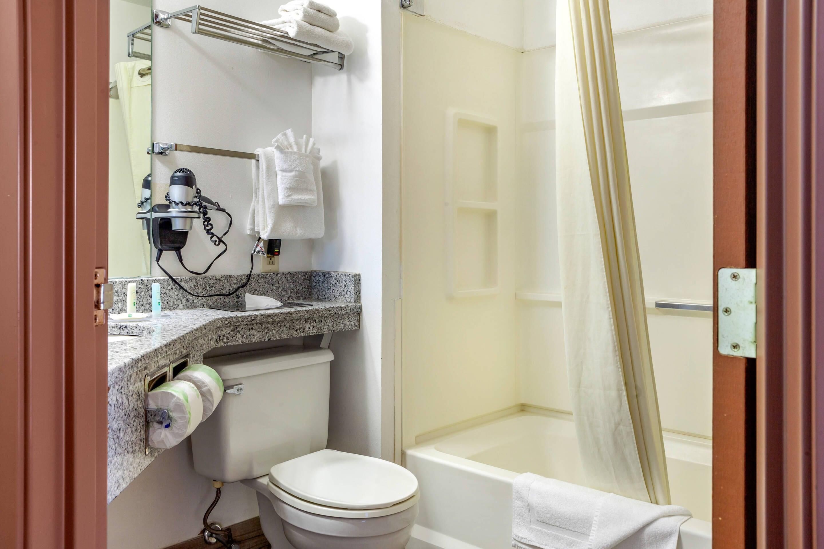 Ein Badezimmer mit Toilette, Waschbecken, Haartrockner, Handtuchhalter und Duschvorhang.
