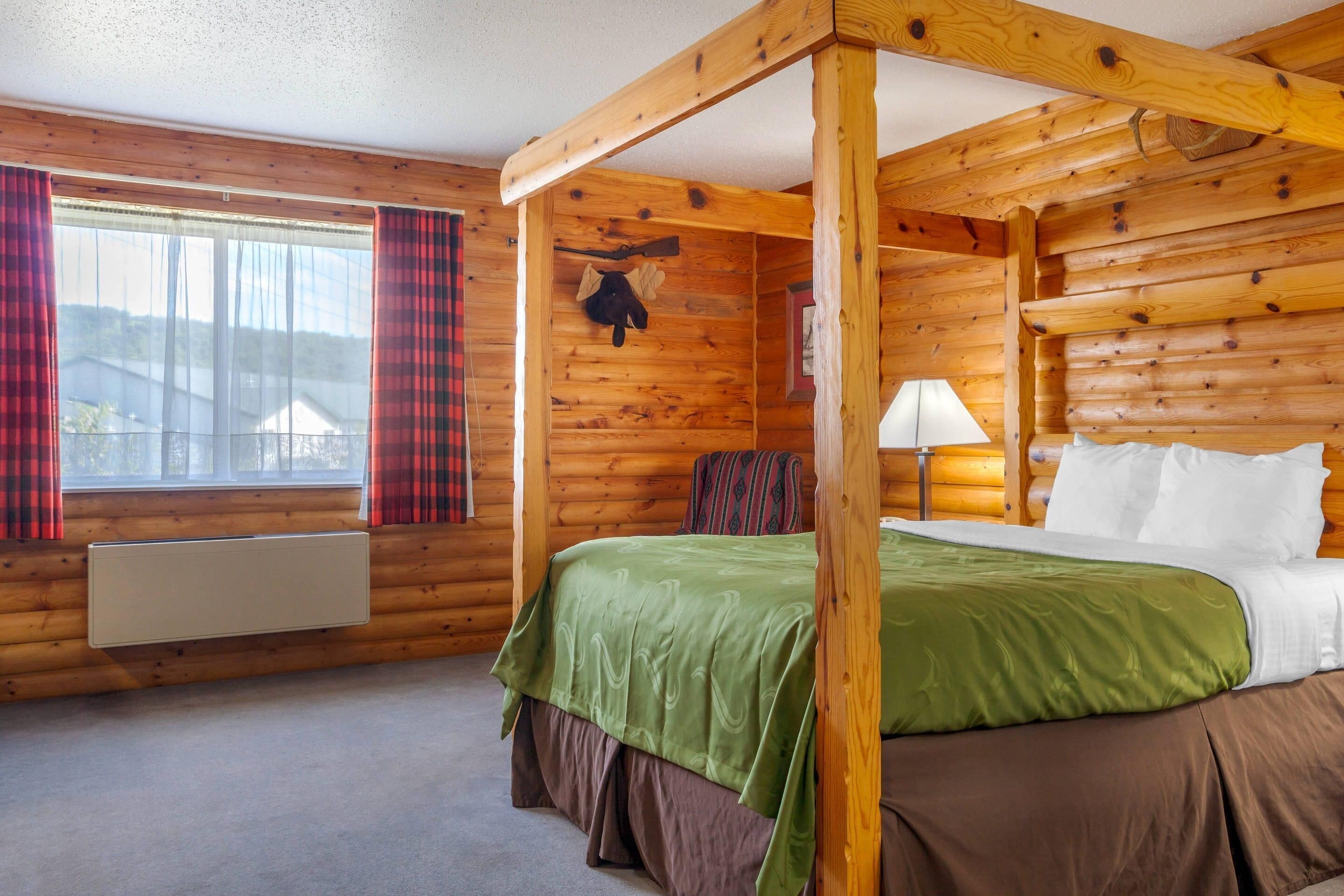 A wooden cabin room with a bed, a window with curtains, a mounted coat, and a radiator.