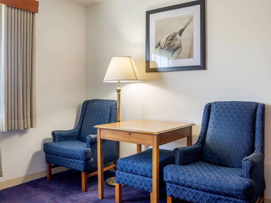 A room with two blue armchairs, a wooden table, a floor lamp, a radiator, and a framed picture on the wall.