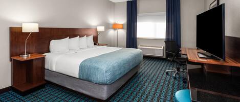 A hotel room with a bed, desk, TV, and patterned carpet.