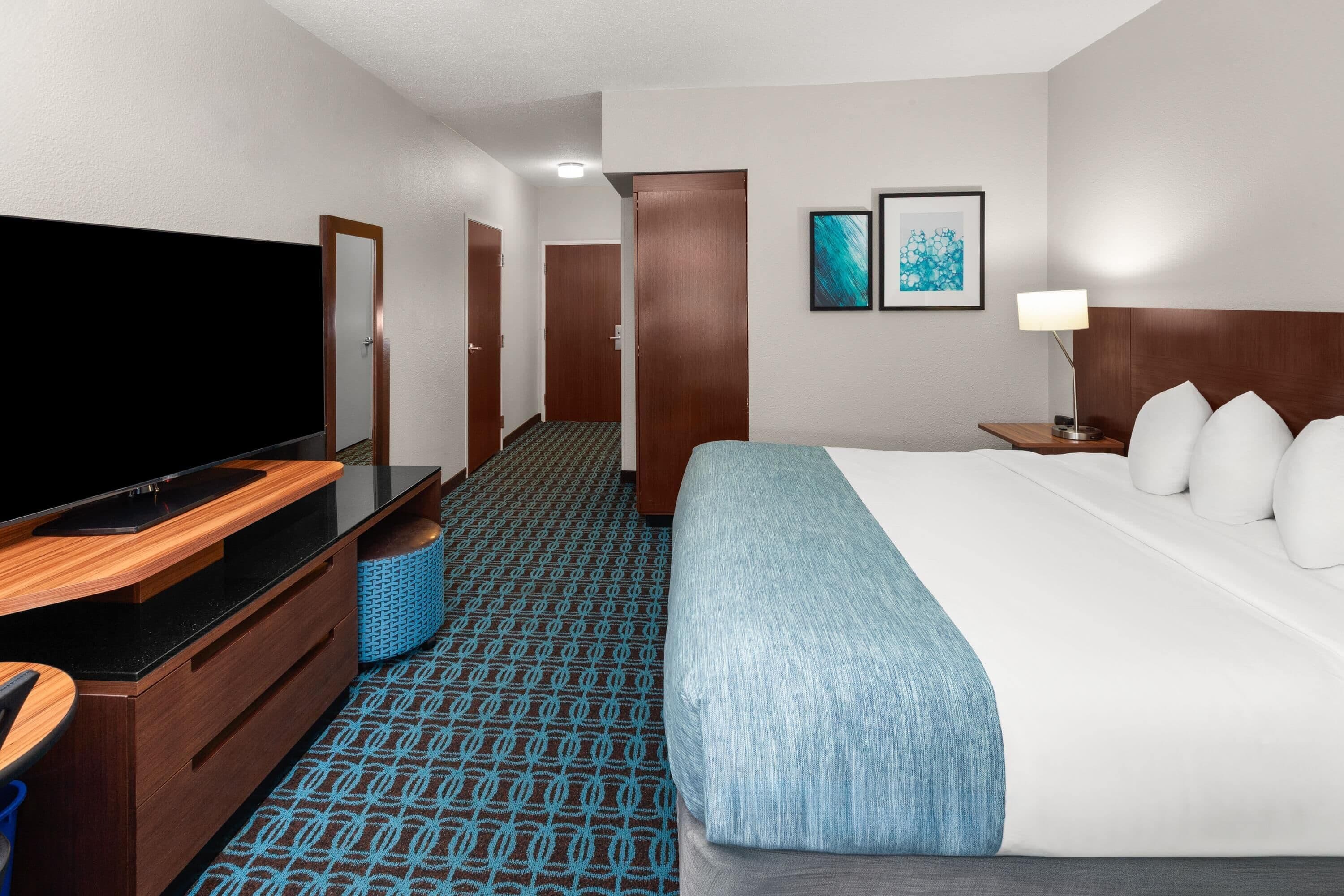 A hotel room with a bed, a TV, a desk, a chair, a lamp, and a door.