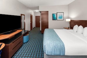 A hotel room with a bed, a TV, a desk, a chair, a lamp, and a door. - Wingate by Wyndham Oshkosh (Oshkosh)