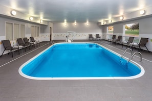 An indoor swimming pool with a blue water feature, surrounded by lounge chairs and a tiled floor. - Wingate by Wyndham Oshkosh (Oshkosh)