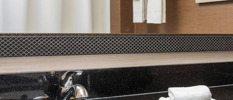 A bathroom with a black granite sink, a white towel rack with folded towels, a shower curtain, and a framed picture on the wall.