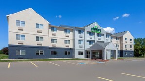 A multi-story hotel with a prominent sign, a parking lot, and a covered entrance. - Wingate by Wyndham Oshkosh (Oshkosh)