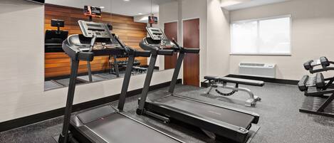 A gym with treadmills, a bench press, and a wall-mounted TV.