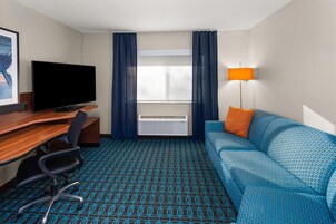 Una habitación de hotel con escritorio, televisor, sofá y ventana con cortinas.