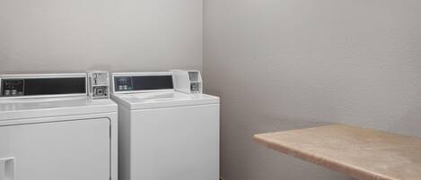 A laundry area with two white washing machines and a beige shelf.