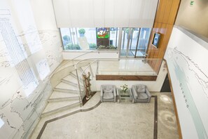 Un interior moderno con suelo de mármol, una escalera, asientos grises y un gran ventanal con vistas al exterior.