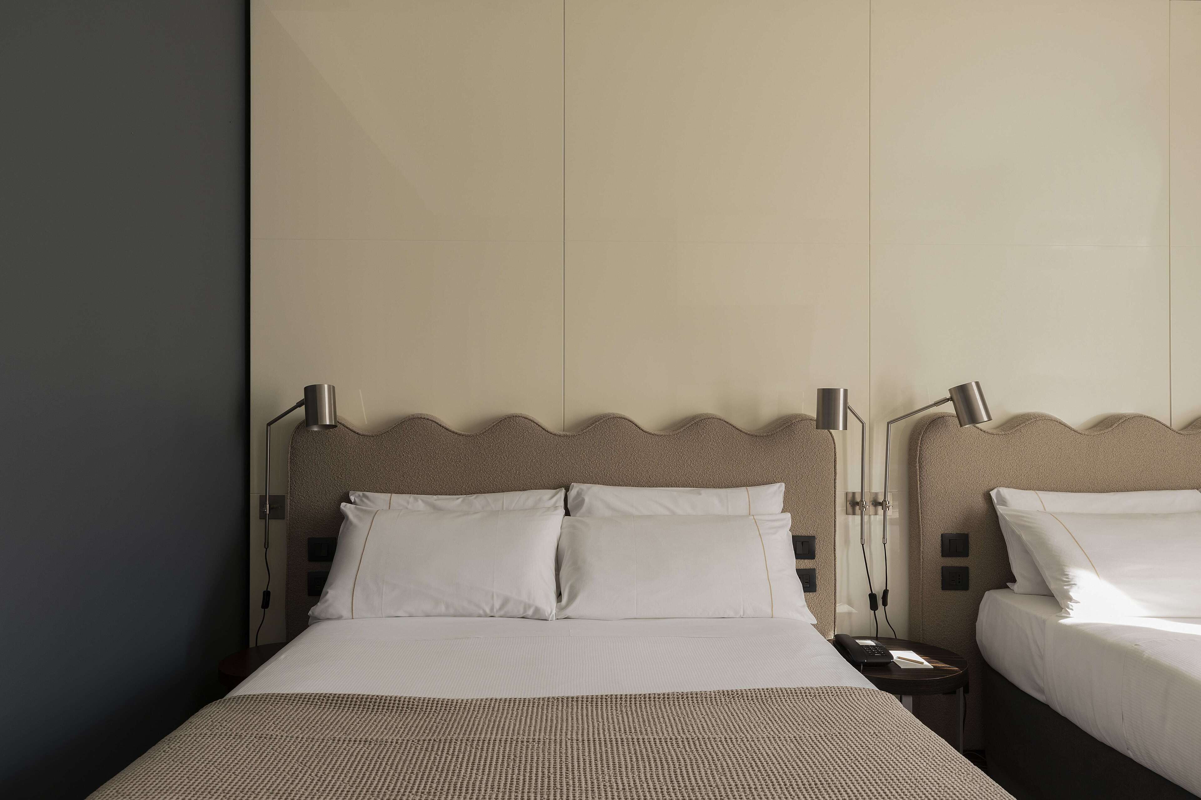 A hotel room with two beds, a large window, and a nightstand with a lamp.