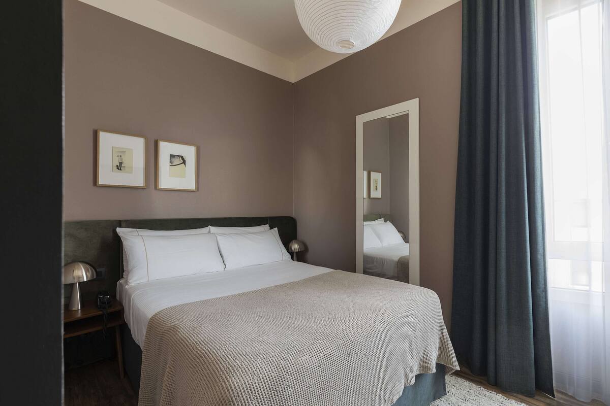 A neatly made bed with a white comforter and pillows, a bedside lamp, and two framed pictures on the wall.