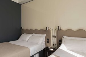 Een hotelkamer met twee bedden, een donkere muur en een lichtgekleurd hoofdeinde.