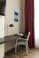A hotel room with a desk, a chair, a TV mounted on the wall, and two framed pictures.