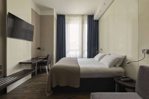 Camera d'albergo moderna con un letto, una scrivania, una sedia, una TV a parete e una finestra con tende.