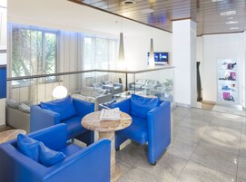 Una hall moderna con sedute blu, ringhiera in vetro, televisore a parete e vetrina per scarpe.