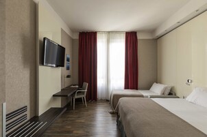 Een hotelkamer met een flatscreen televisie aan de muur, een bureau met een stoel, twee bedden en een raam met rode gordijnen.