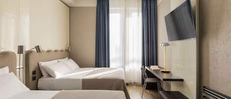 A hotel room with two beds, a desk, a TV, and a window with curtains.