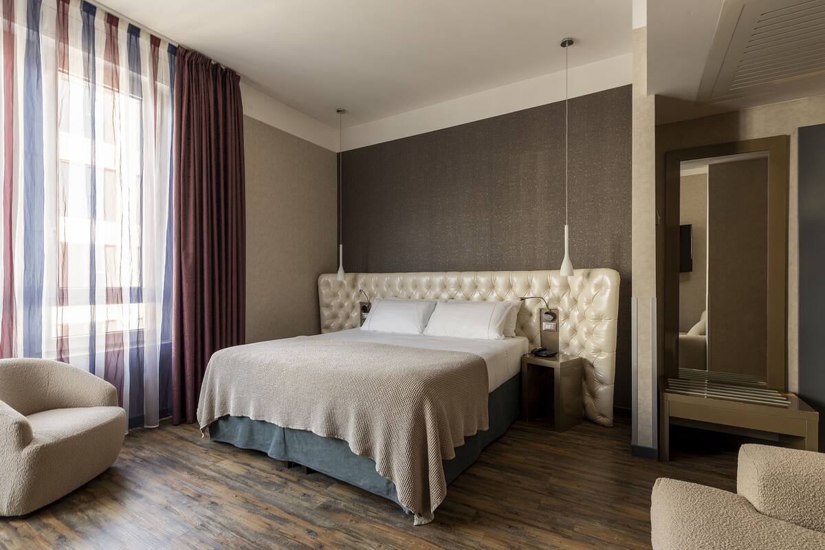 A hotel room with a large bed, a chair, a bedside table, and a wardrobe.