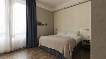 Una habitación de hotel moderna con una cama grande, una mesita de noche y una ventana con cortinas translúcidas.