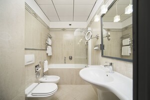 A modern bathroom with a bathtub, two sinks, a toilet, and a large mirror.
