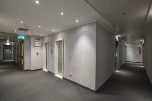 A corridor with doors, emergency exit signs, and a fire alarm.