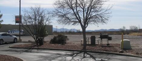 A parking lot with a white car, a bench, a mailbox, and a trash can.