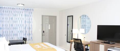 A hotel room with a bed, desk, chair, television, and a mirror.