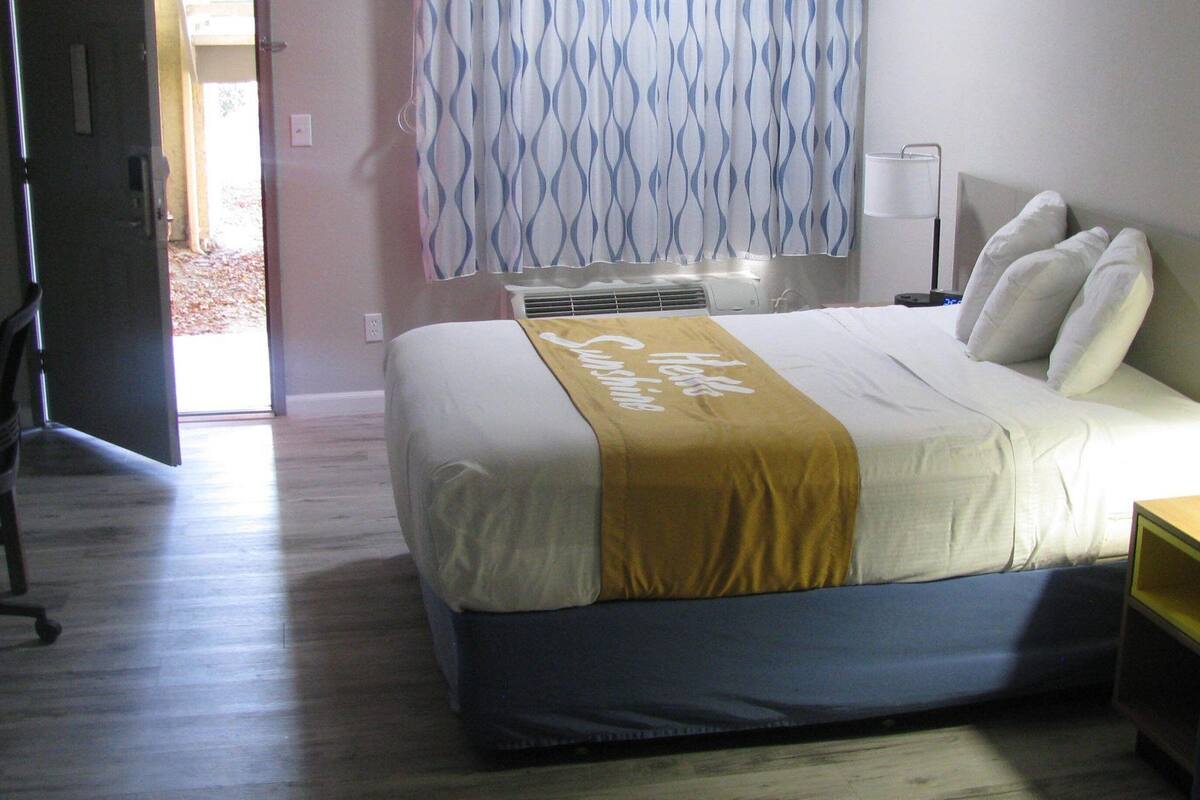 Ein Hotelzimmer mit Bett, Nachttisch, Lampe und Blick ins Freie.