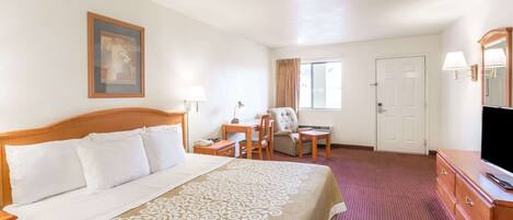 A hotel room with a bed, desk, chair, TV, and a door.