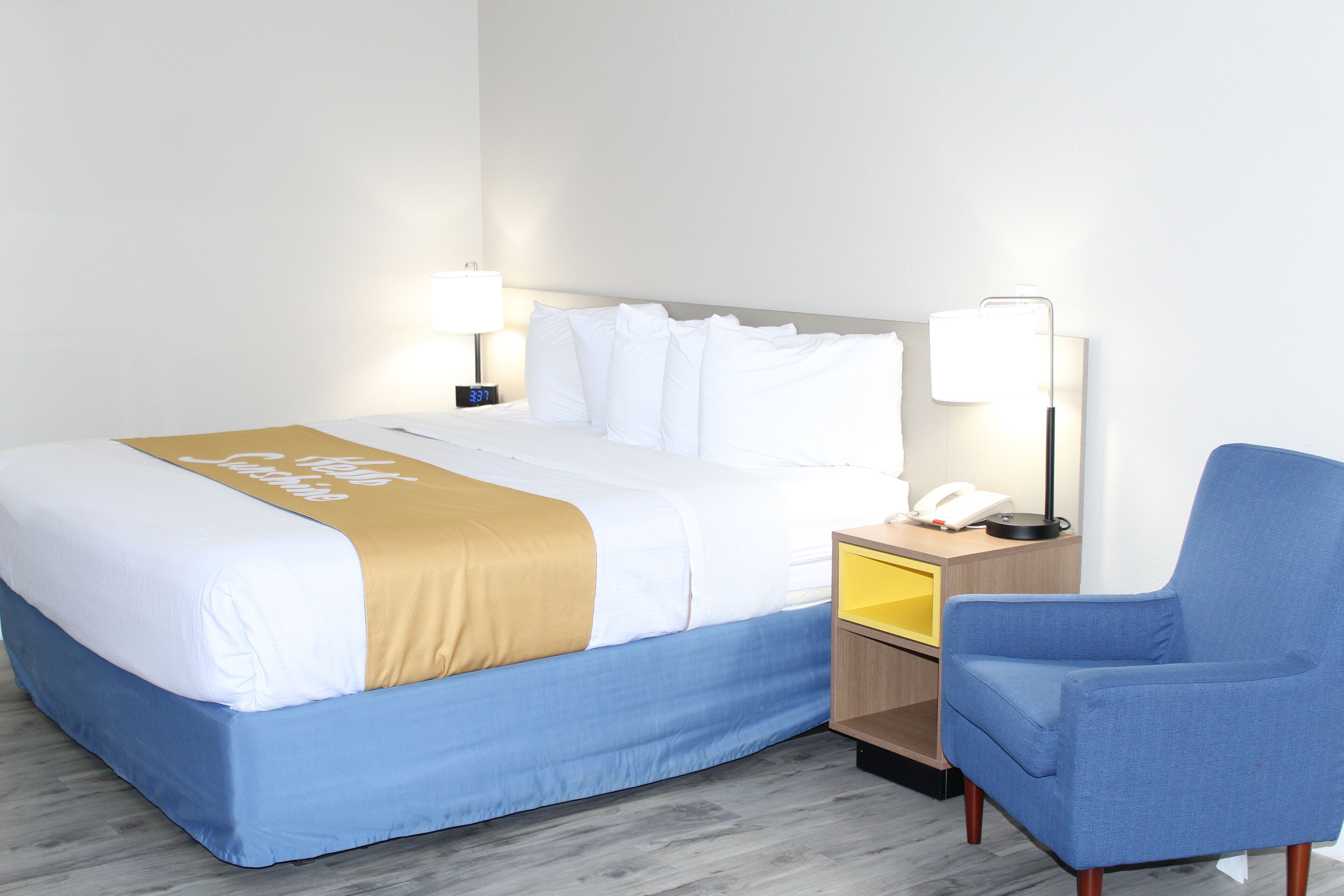 Una habitación de hotel con una cama, una silla, una mesita de noche con lámpara y teléfono.