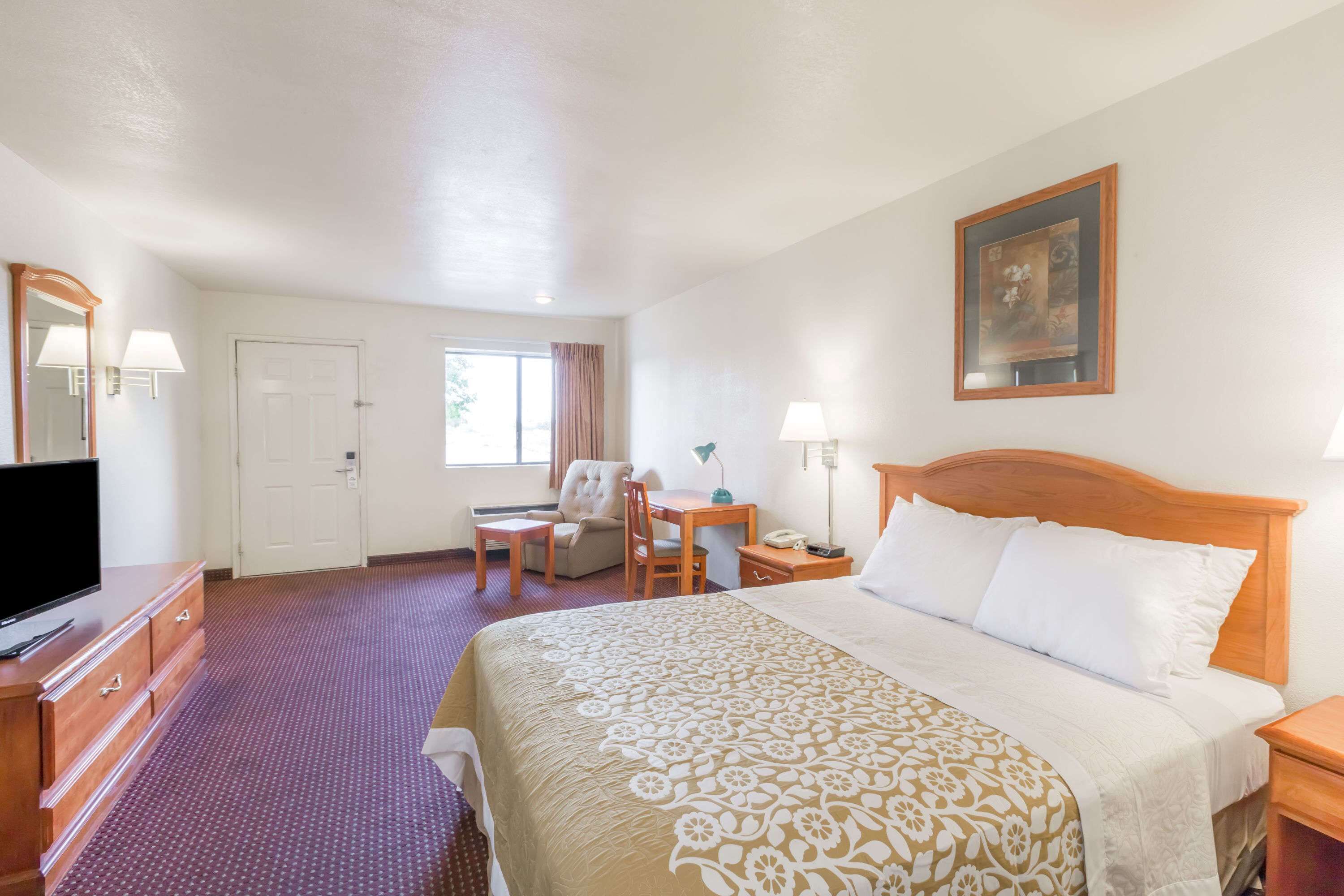 A hotel room with a bed, a desk, a chair, a television, and a painting on the wall.