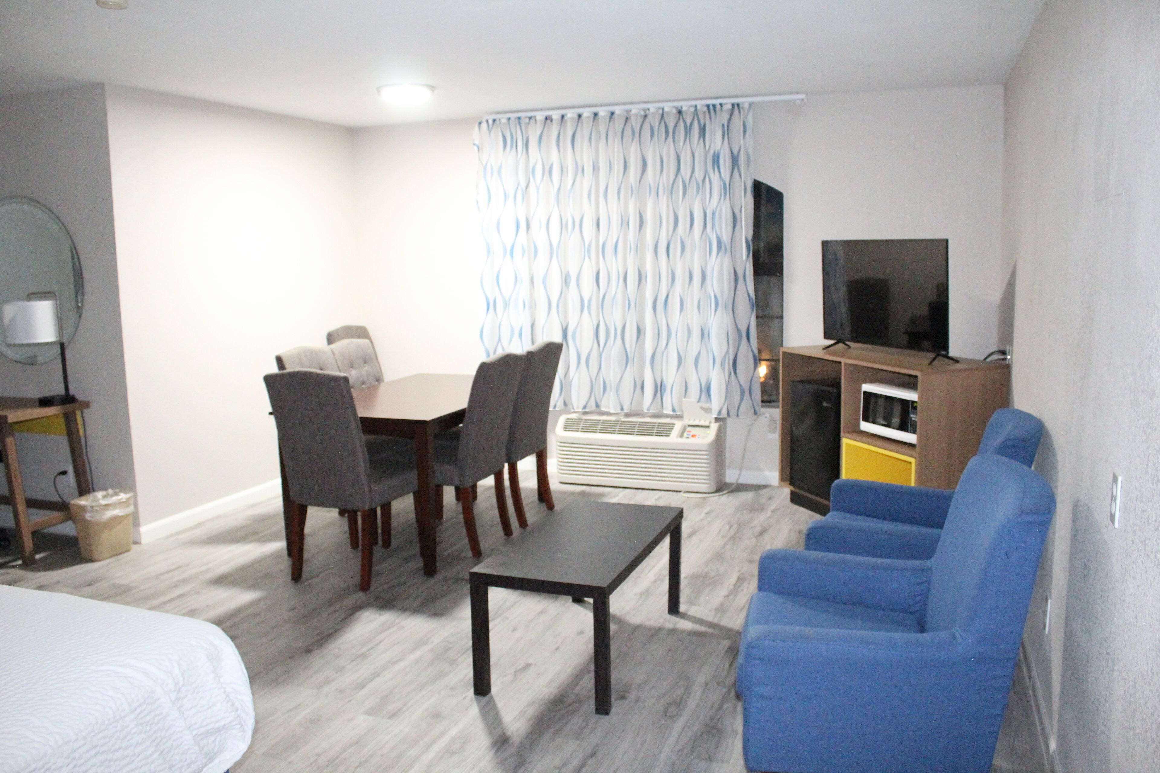 Een compacte hotelkamer met een bed, een klein tafeltje, een blauwe fauteuil, een eethoek met stoelen, een televisie en een magnetron.