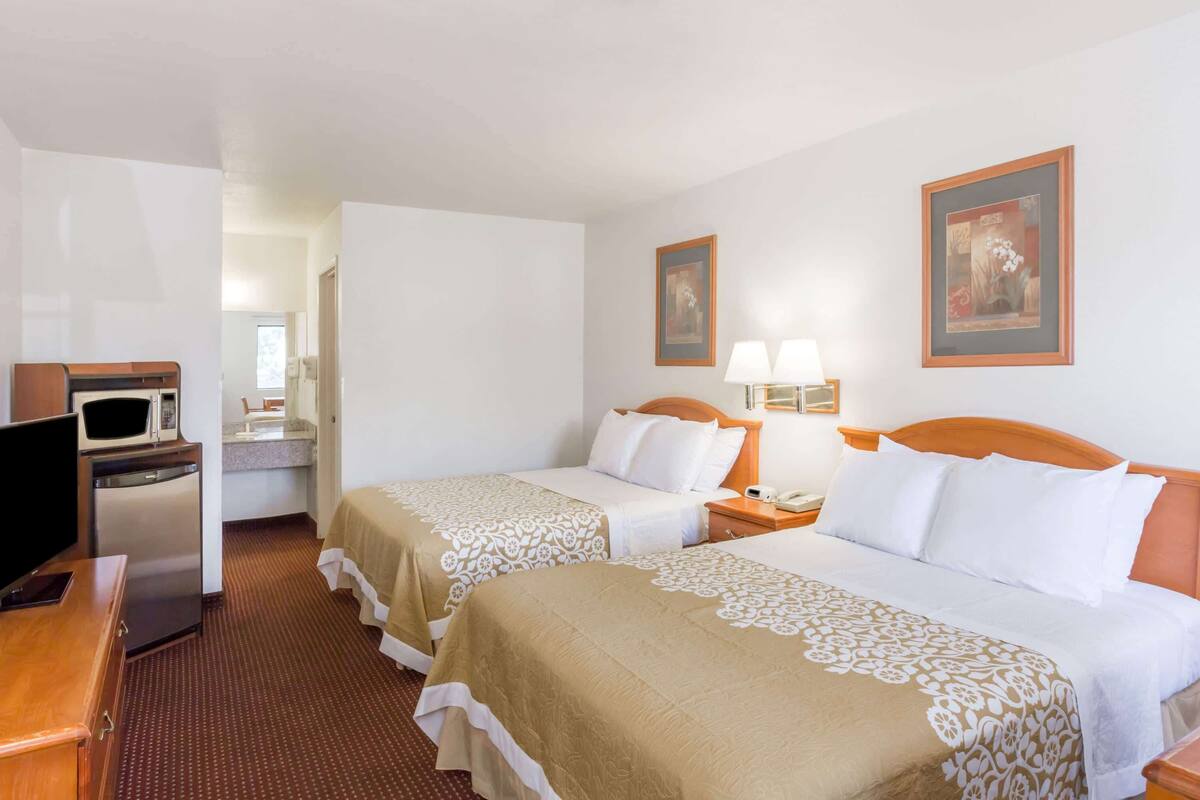 Ein Hotelzimmer mit zwei Betten, einem Schreibtisch, einem Fernseher, einer Mikrowelle und einem kleinen Badezimmer.