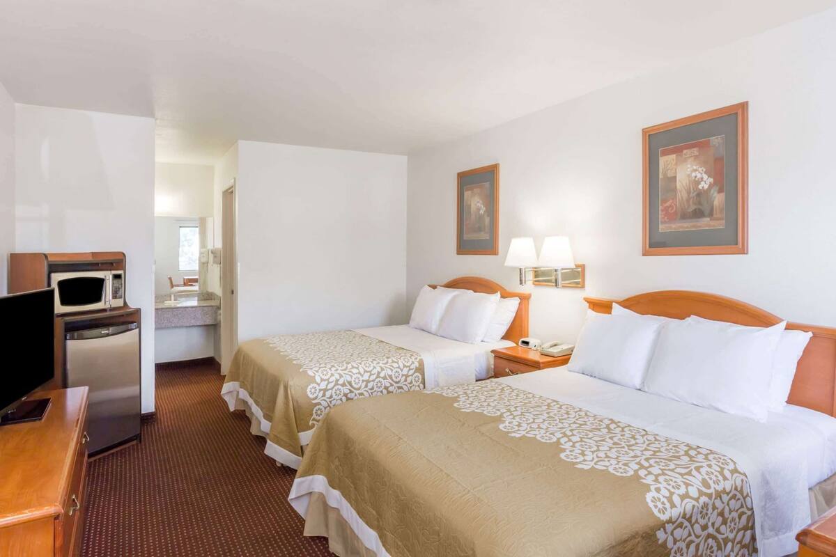 Ein Hotelzimmer mit zwei Betten, einer Mikrowelle, einem Fernseher, einem Schreibtisch und einer kleinen Küchenzeile.